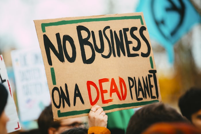 Climate protester holding sign reading "No Business on a Dead Planet," highlighting the urgency of environmental action.